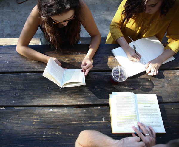 Drei junge Frauen setzen an einem Tisch und lesen.
