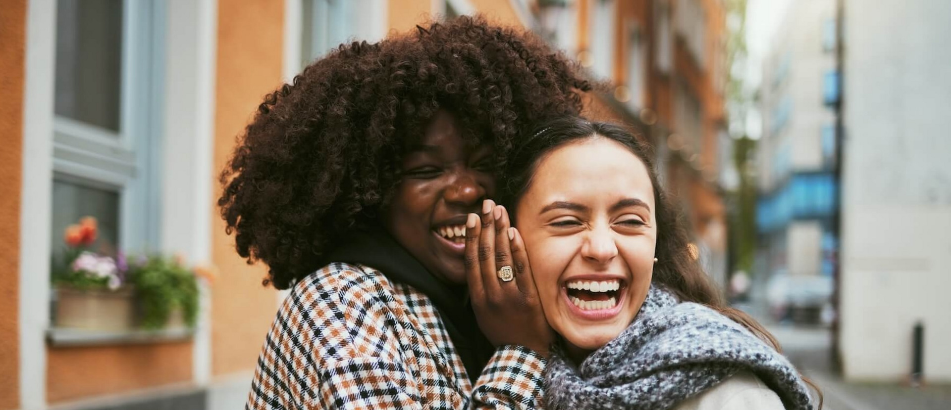 Eine junge Frau flüstert einer Freundin etwas ins Ohr, sie lacht