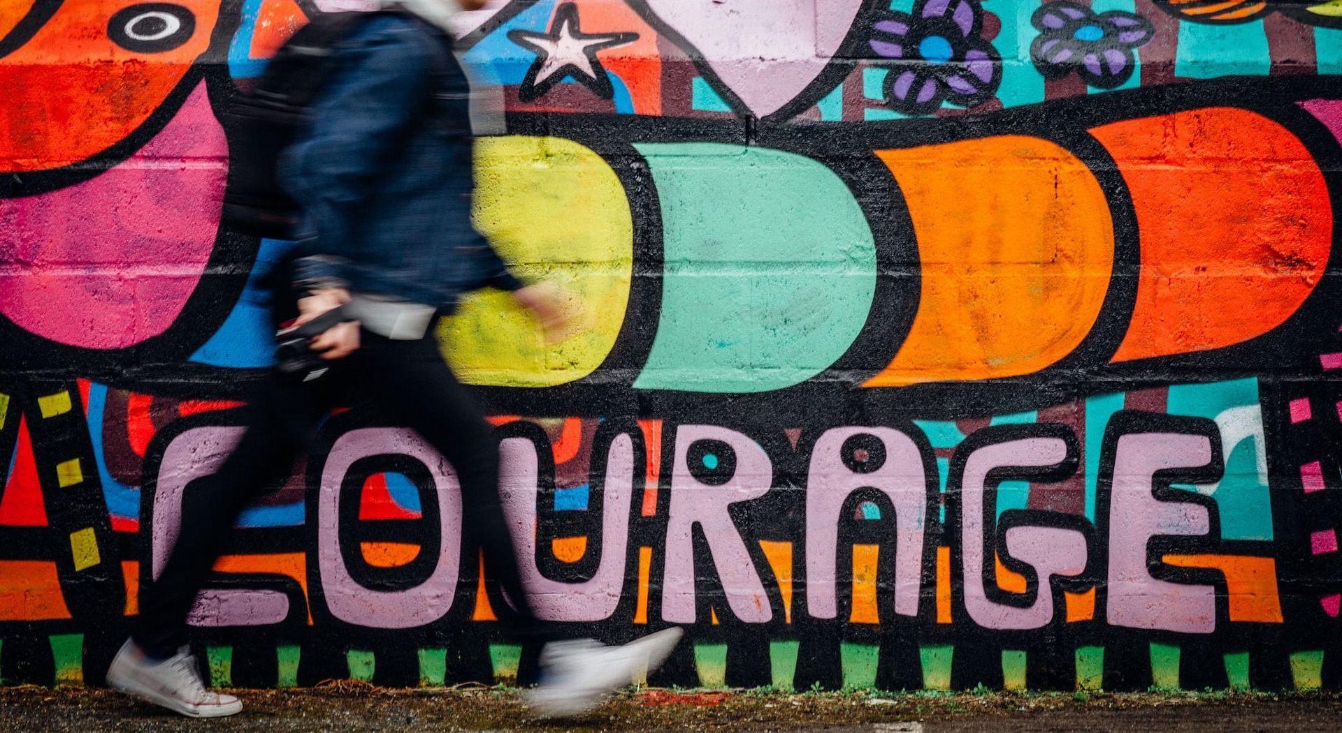 Eine Person läuft an einer Wand vorbei, auf der "Courage" steht