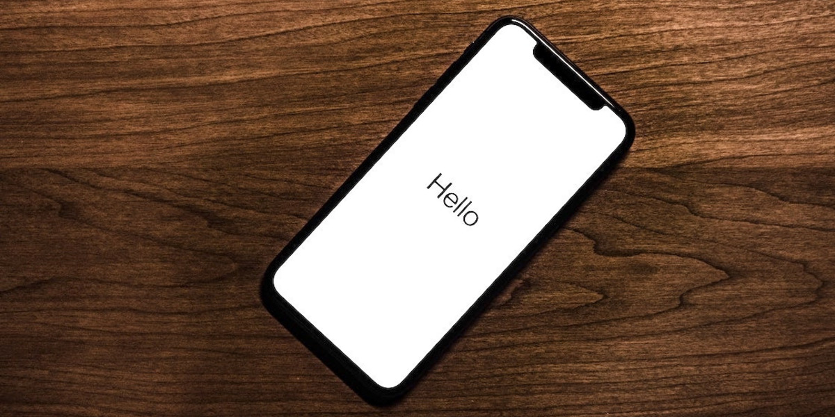 Ein Smartphone mit dem Text "Hello" auf dem Schirm liegt auf einem Holztisch.