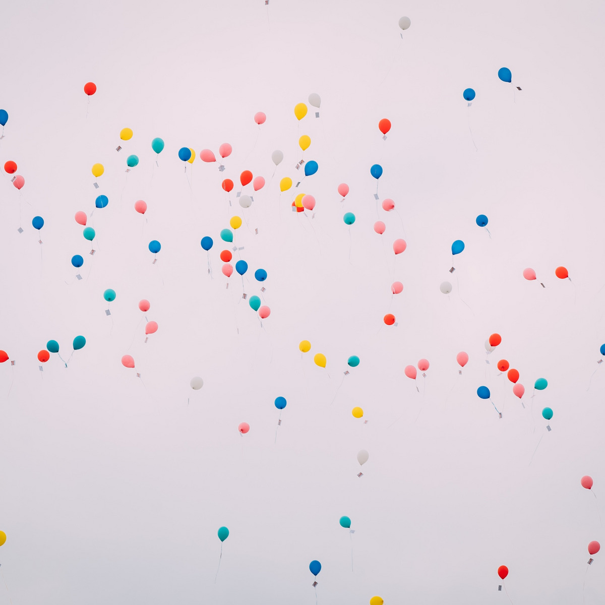 Blick in einen hellgrauen Himmel in dem zahlreiche bunte Luftballons schweben.