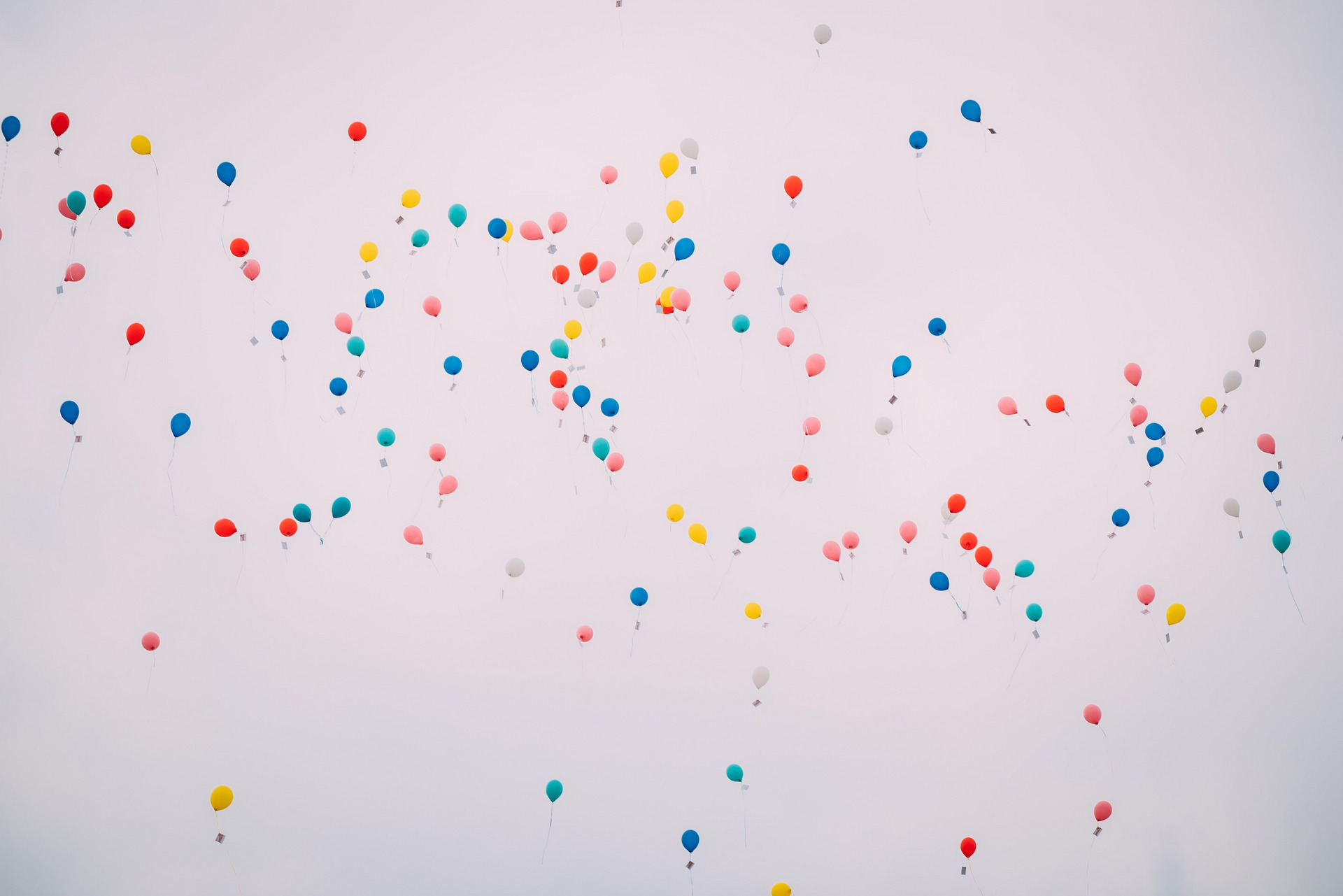 Blick in einen hellgrauen Himmel in dem zahlreiche bunte Luftballons schweben.