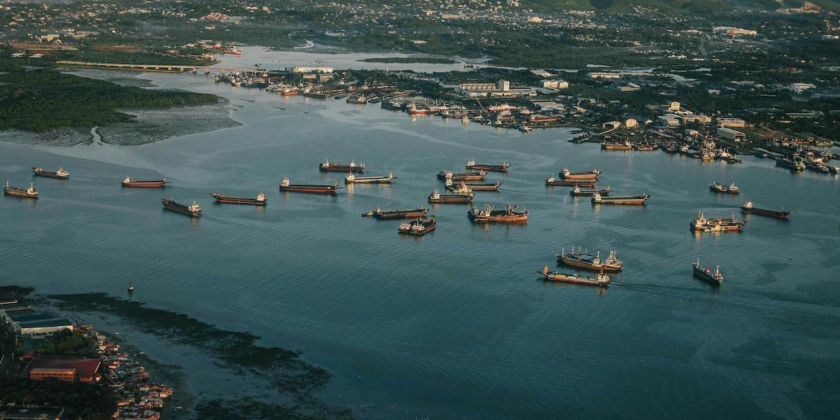 Eine Luftaufnahme von mehreren Containerschiffen, die auf ruhigen Gewässern in einem Hafen nebeneinander liegen.