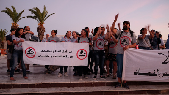 Mehrere Personen demonstrieren mit Transparent vor Palmen