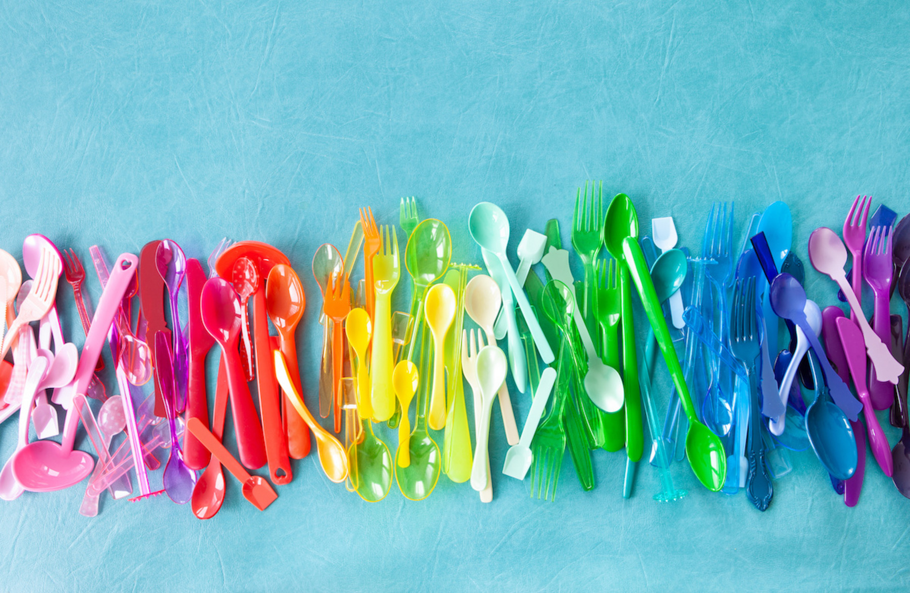 Einwegartikel aus Plastik in Regenbogenfarben auf einem blauen Hintergrund.