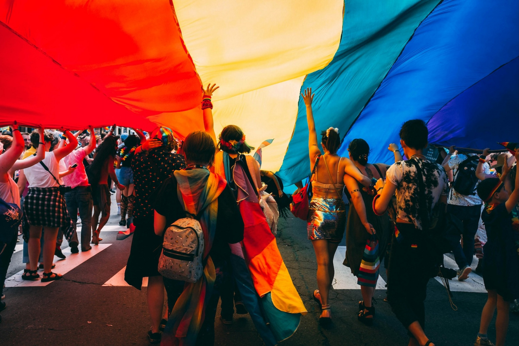 Zu sehen sind Menschen, die unter einer Regenbogenflagge feiern