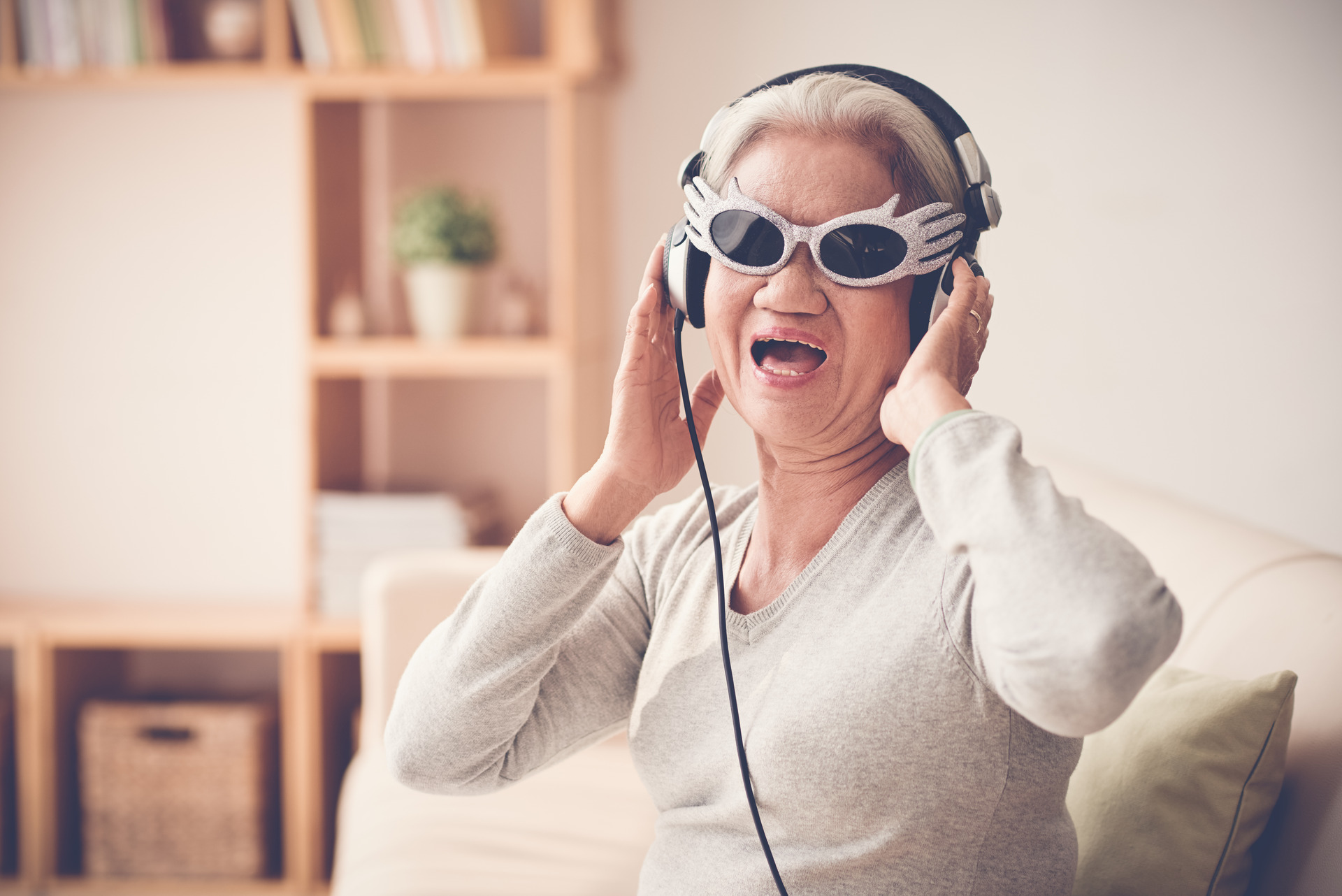 Eine ältere Frau trägt Brille und Kopfhörer und singt.