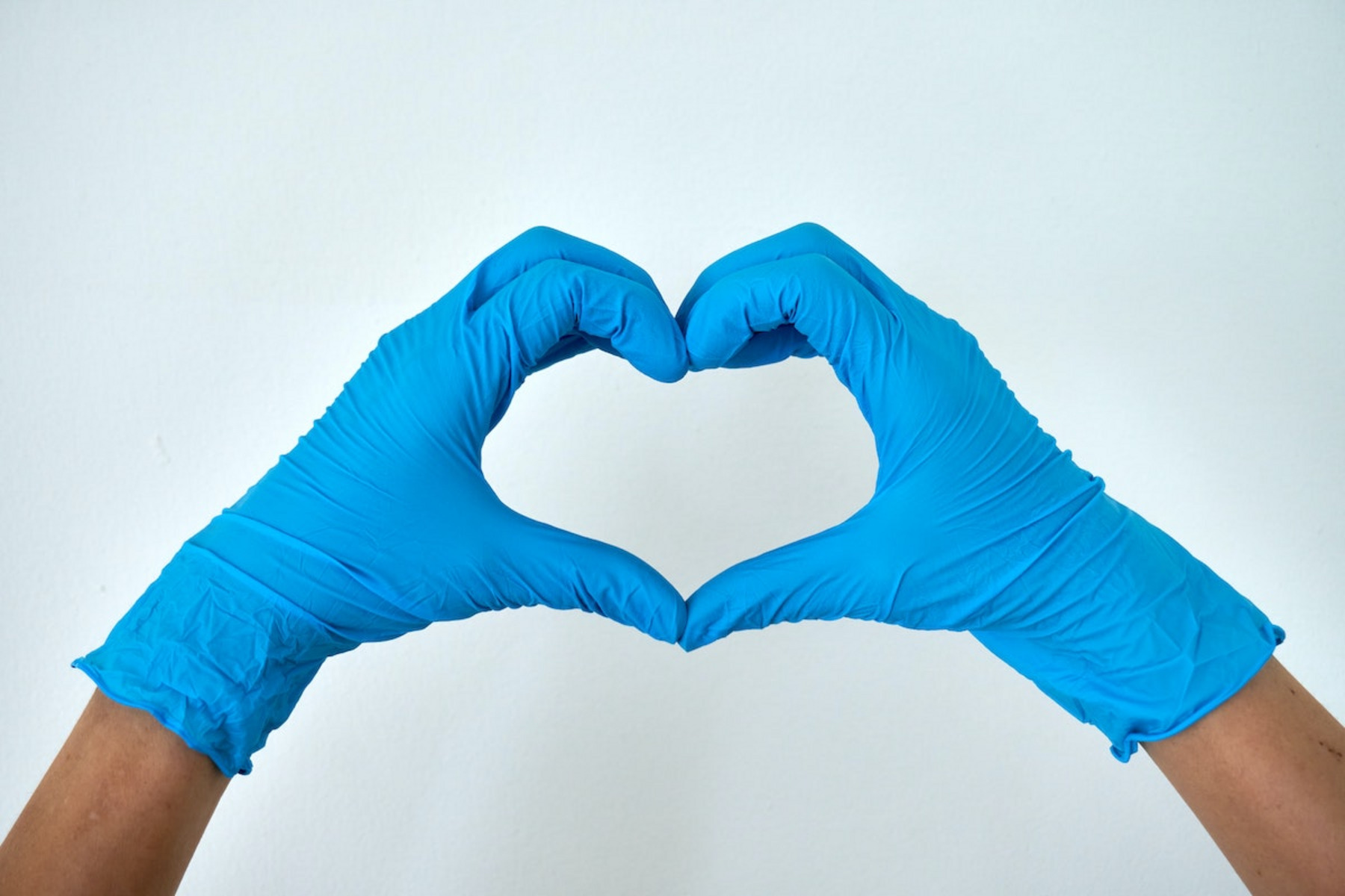 Zwei Hände mit blauen Plastikhandschuhe formen ein Herz mit den Fingern.