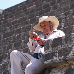 Mann mit Strohhut sitzt auf einer Treppe mit einer Flasche in den Händen