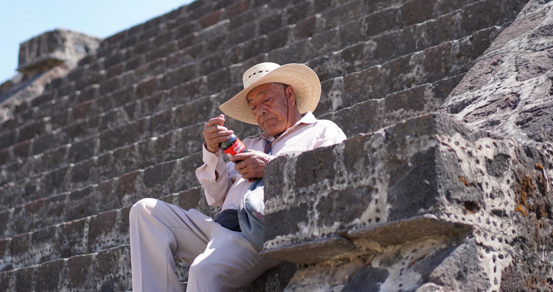 Mann mit Strohhut sitzt auf einer Treppe mit einer Flasche in den Händen