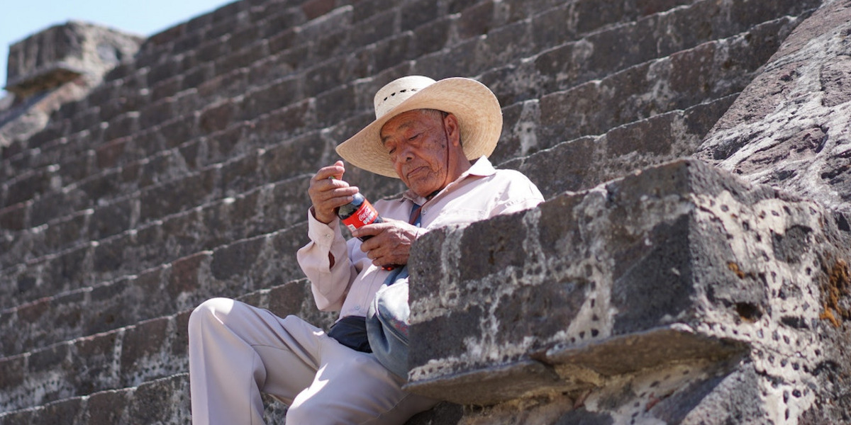 Mann mit Strohhut sitzt auf einer Treppe mit einer Flasche in den Händen