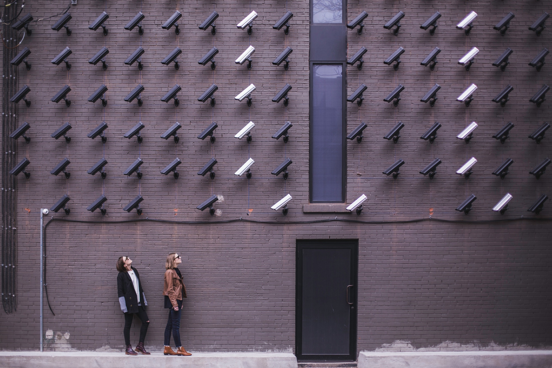Zwei Personen stehen vor einer Wand mit Überwachungskameras