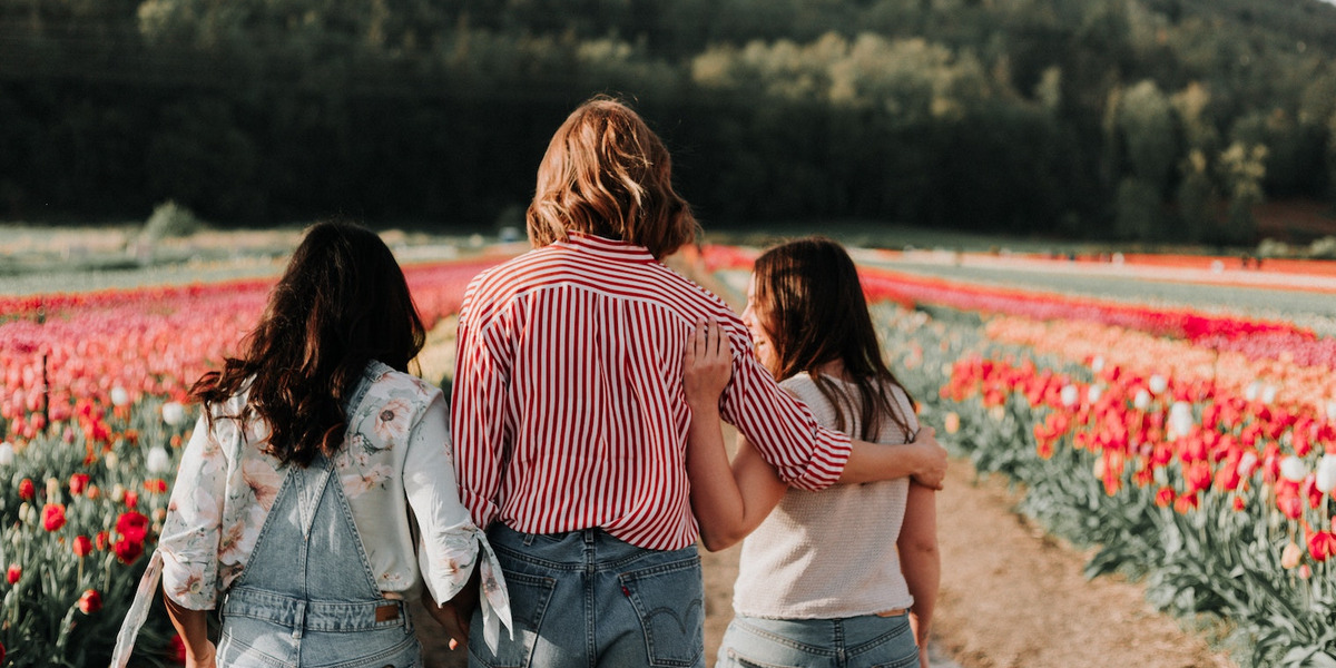Drei junge Frauen stehen vor einem Tulpenfeld und reden vertieft miteinander.