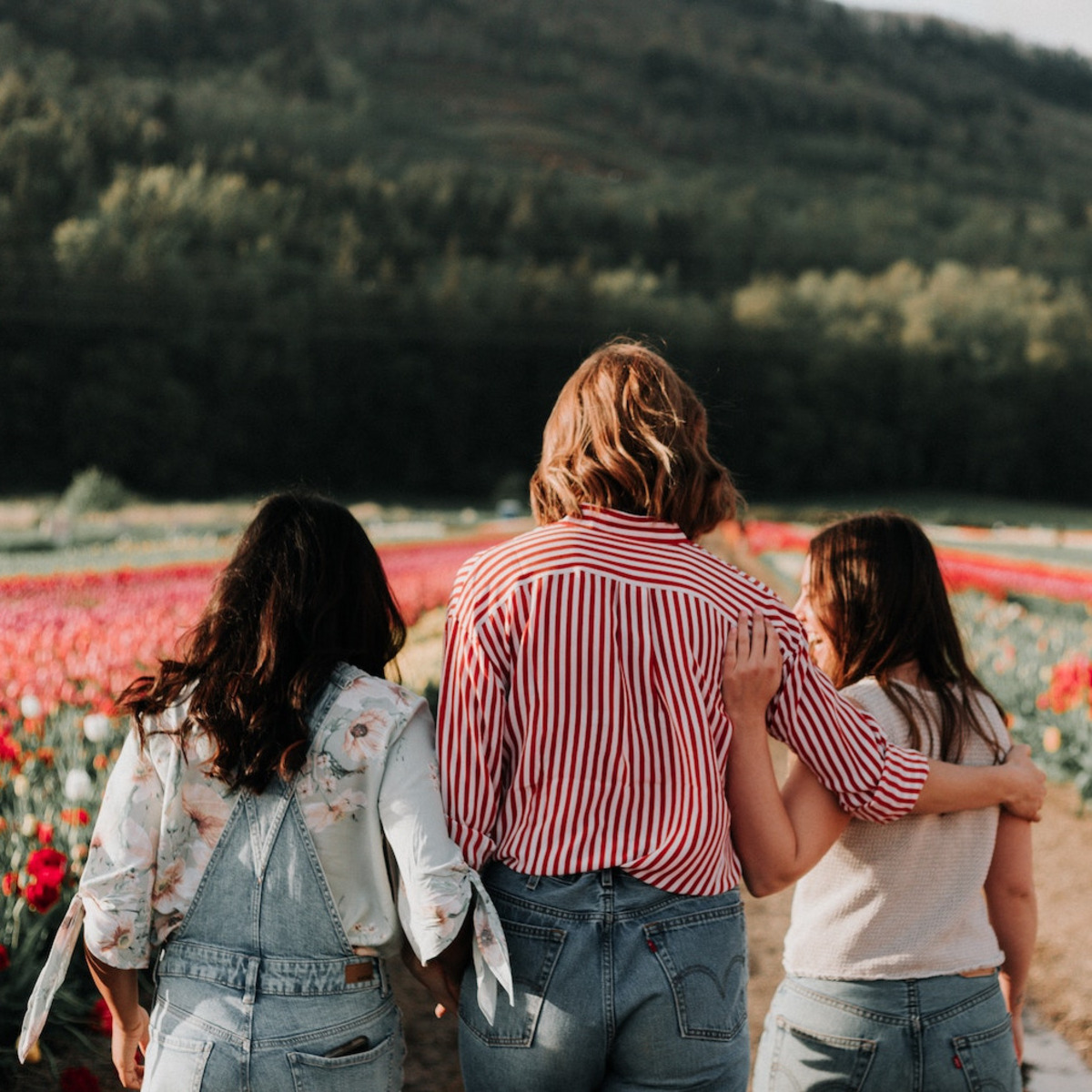 Drei junge Frauen stehen vor einem Tulpenfeld und reden vertieft miteinander.