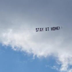 Ein Flugzeug mit einer Banderole hinter sich mit dem Text "STAY AT HOME!"