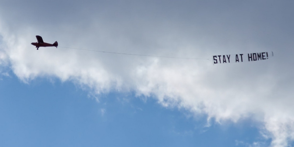 Ein Flugzeug mit einer Banderole hinter sich mit dem Text "STAY AT HOME!"
