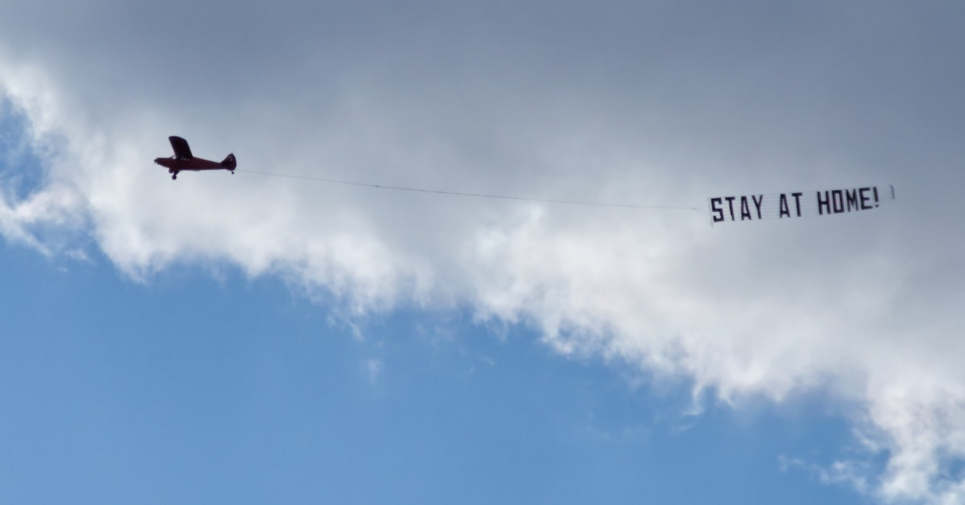 Ein Flugzeug mit einer Banderole hinter sich mit dem Text "STAY AT HOME!"