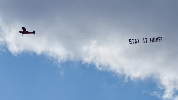 Ein Flugzeug mit einer Banderole hinter sich mit dem Text "STAY AT HOME!"