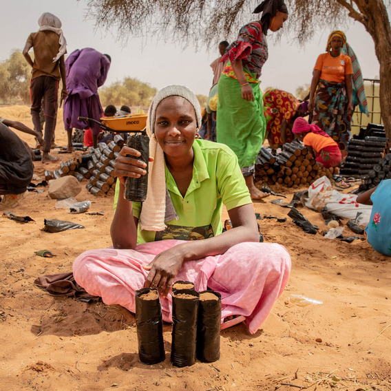 Menschen bei der Arbeit in einer ländlichen Gegend im Senegal. Sie schaufeln Erde und Akaziensetzlinge in kleine schwarze Plastiktüten.
