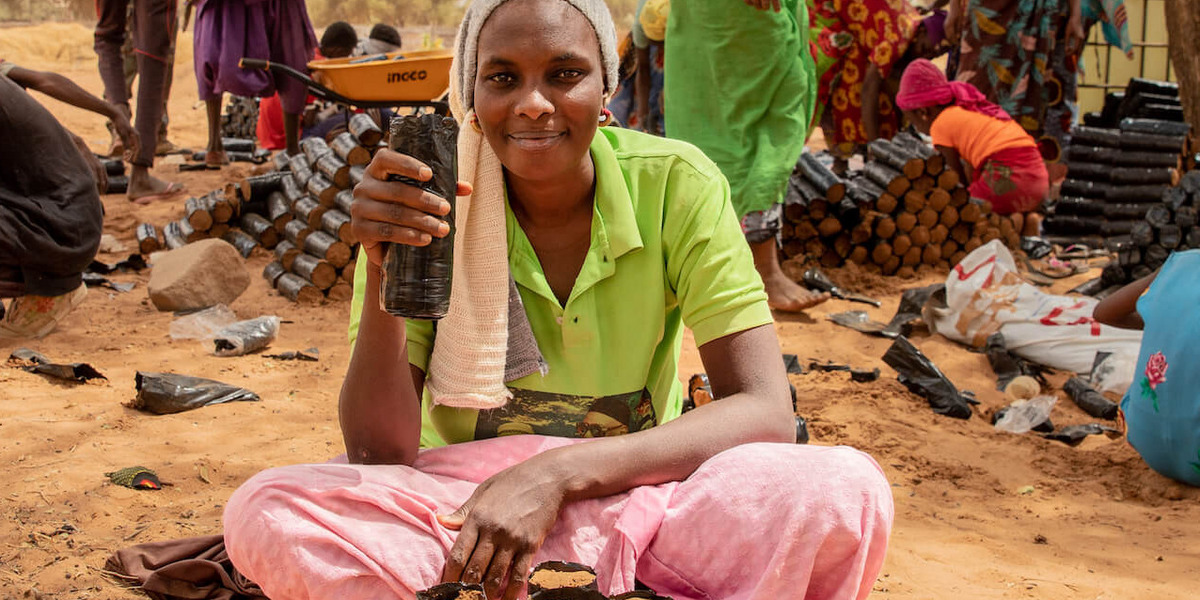 Menschen bei der Arbeit in einer ländlichen Gegend im Senegal. Sie schaufeln Erde und Akaziensetzlinge in kleine schwarze Plastiktüten.