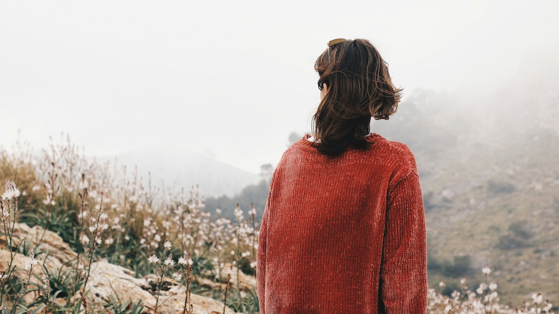 Eine Frau blickt auf eine karge Berglandschaft im Nebel