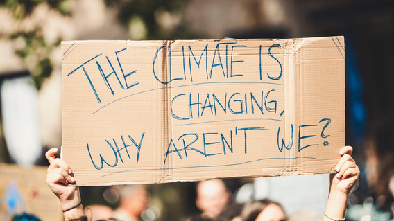 Klimaaktivisten halten ein Plakat hoch: "The climate is changing, why aren't we?"