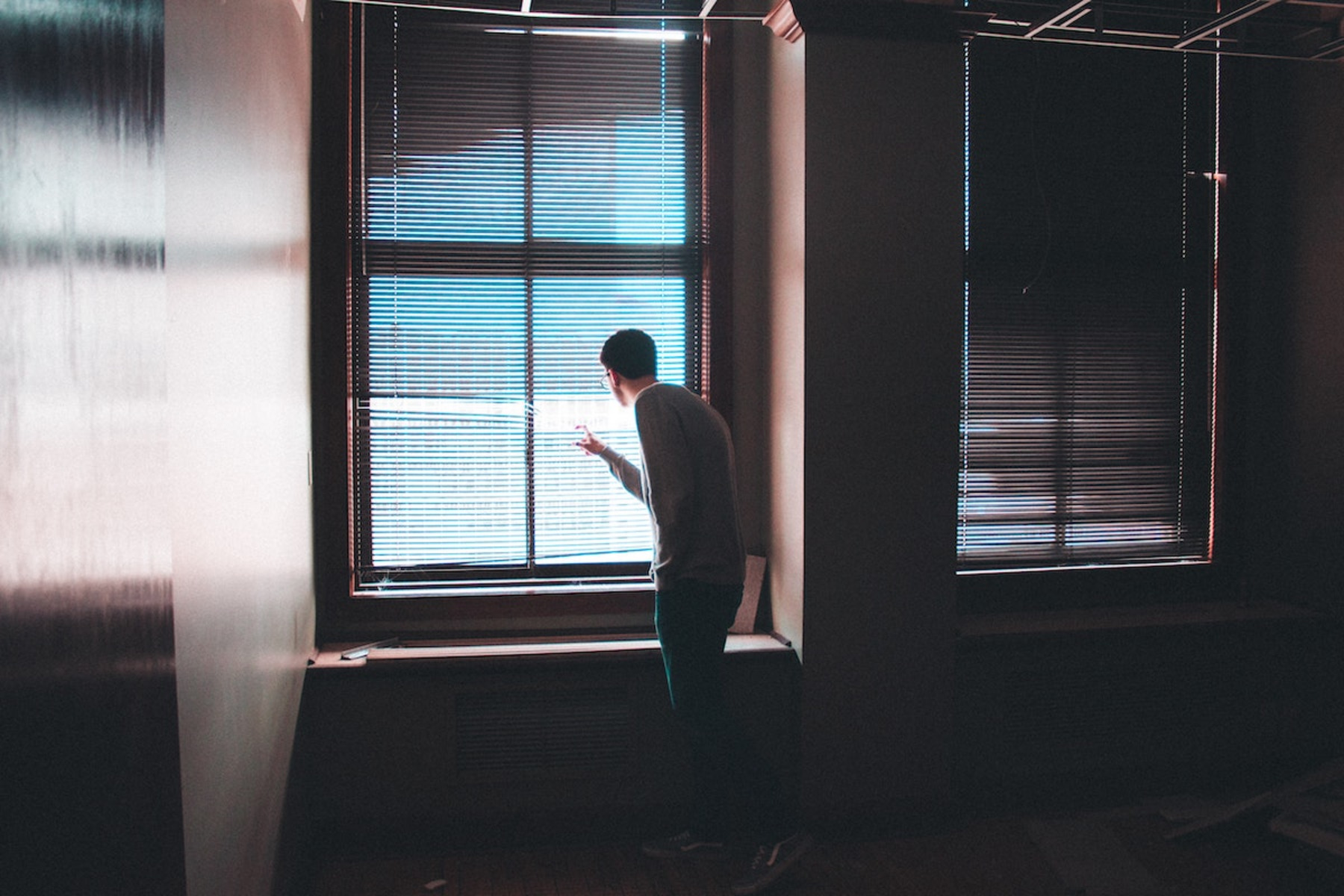 Eine Person schaut durch die Jalousien und aus dem Fenster.