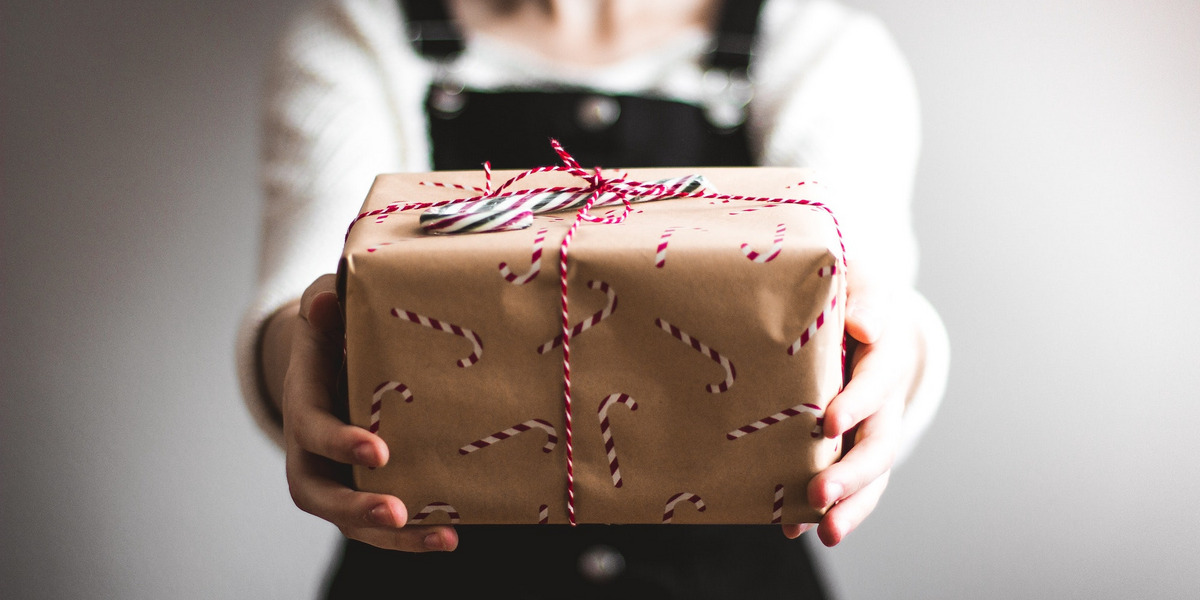 Eine festlich gekleidete Frau hält ein schön verpacktes Geschenk in die Kamera.