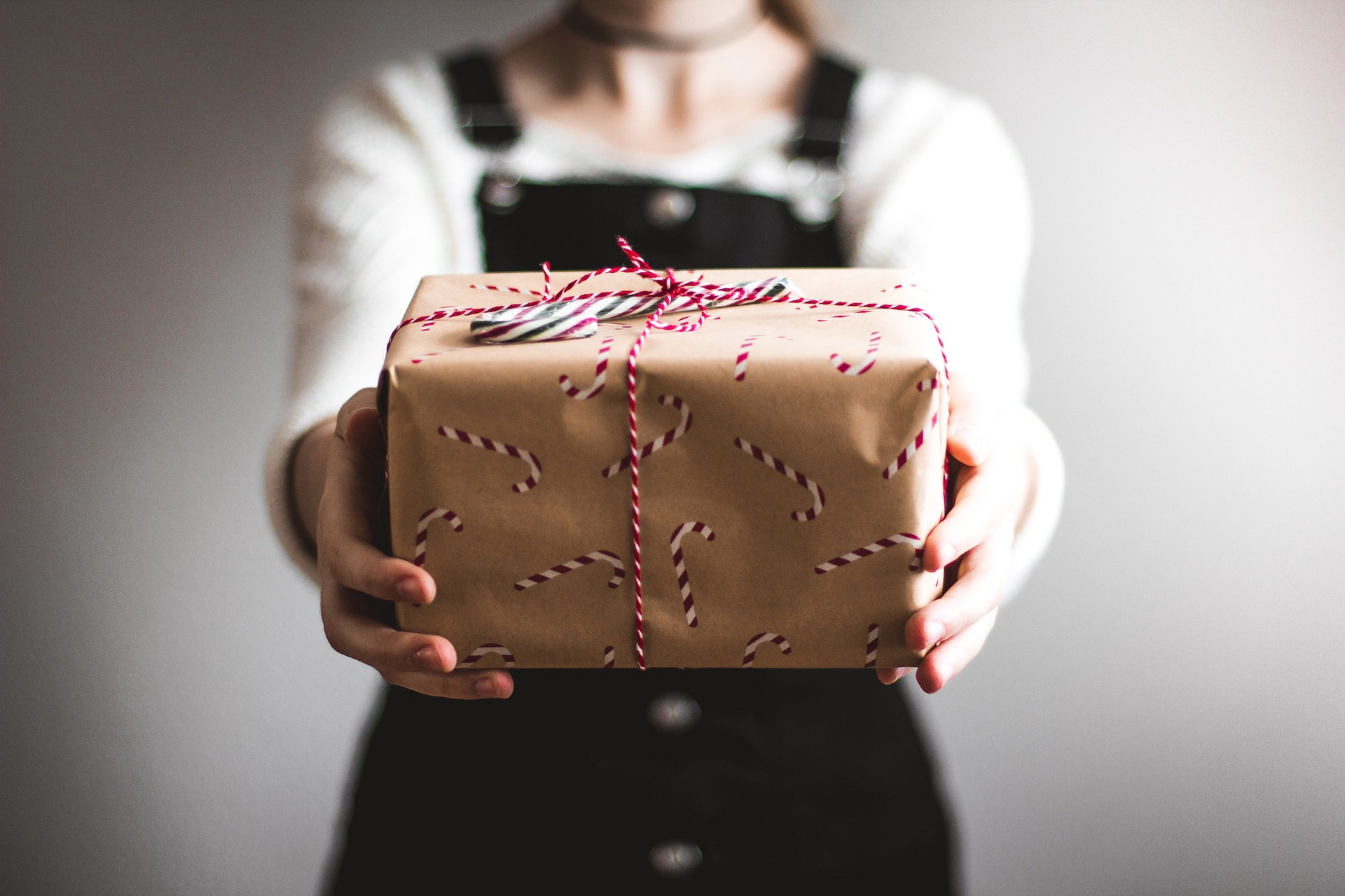 Eine festlich gekleidete Frau hält ein schön verpacktes Geschenk in die Kamera.