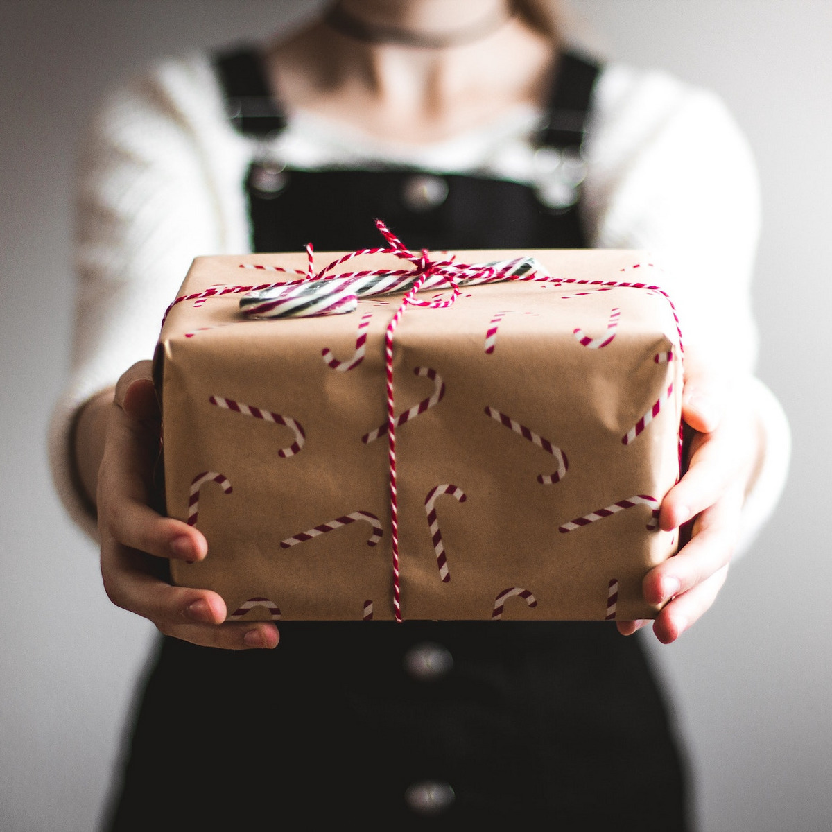 Eine festlich gekleidete Frau hält ein schön verpacktes Geschenk in die Kamera.