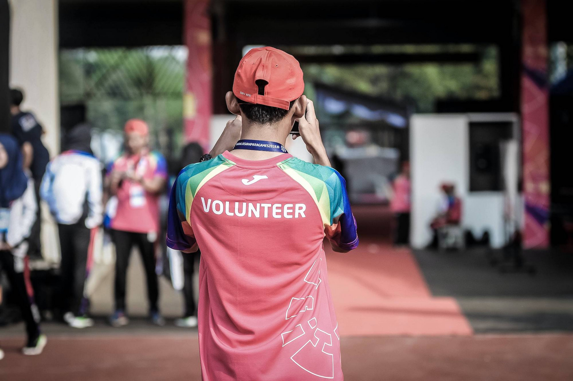 Eine Person mit der Aufschrift "Volunteer" (engl. "Freiwillige:r") steht mit dem Rücken zu uns und schießt ein Foto einer Szene im Hintergrund