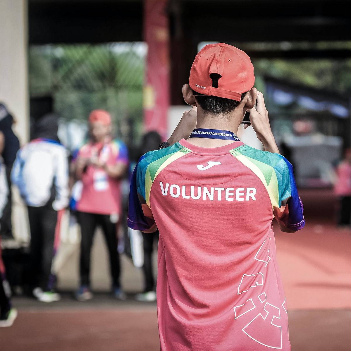 Eine Person mit der Aufschrift "Volunteer" (engl. "Freiwillige:r") steht mit dem Rücken zu uns und schießt ein Foto einer Szene im Hintergrund