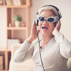 Eine ältere Frau trägt Brille und Kopfhörer und singt.