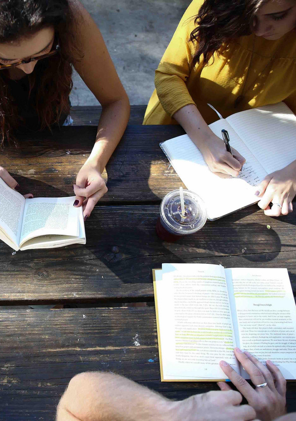 Drei junge Frauen setzen an einem Tisch und lesen.