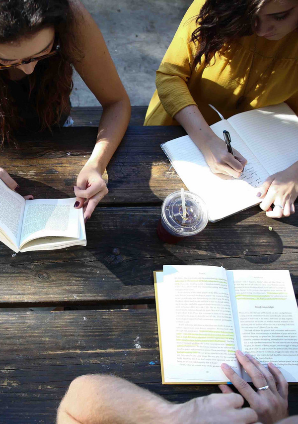 Drei junge Frauen setzen an einem Tisch und lesen.