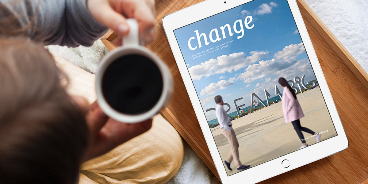 Die neue Ausgabe des change Magazins erscheint auf einem Tablet. Das Gerät liegt auf einem hölzernen Tablett, vor dem eine junge Frau sitzt, die eine Tasse Kaffee in den Händen hält.