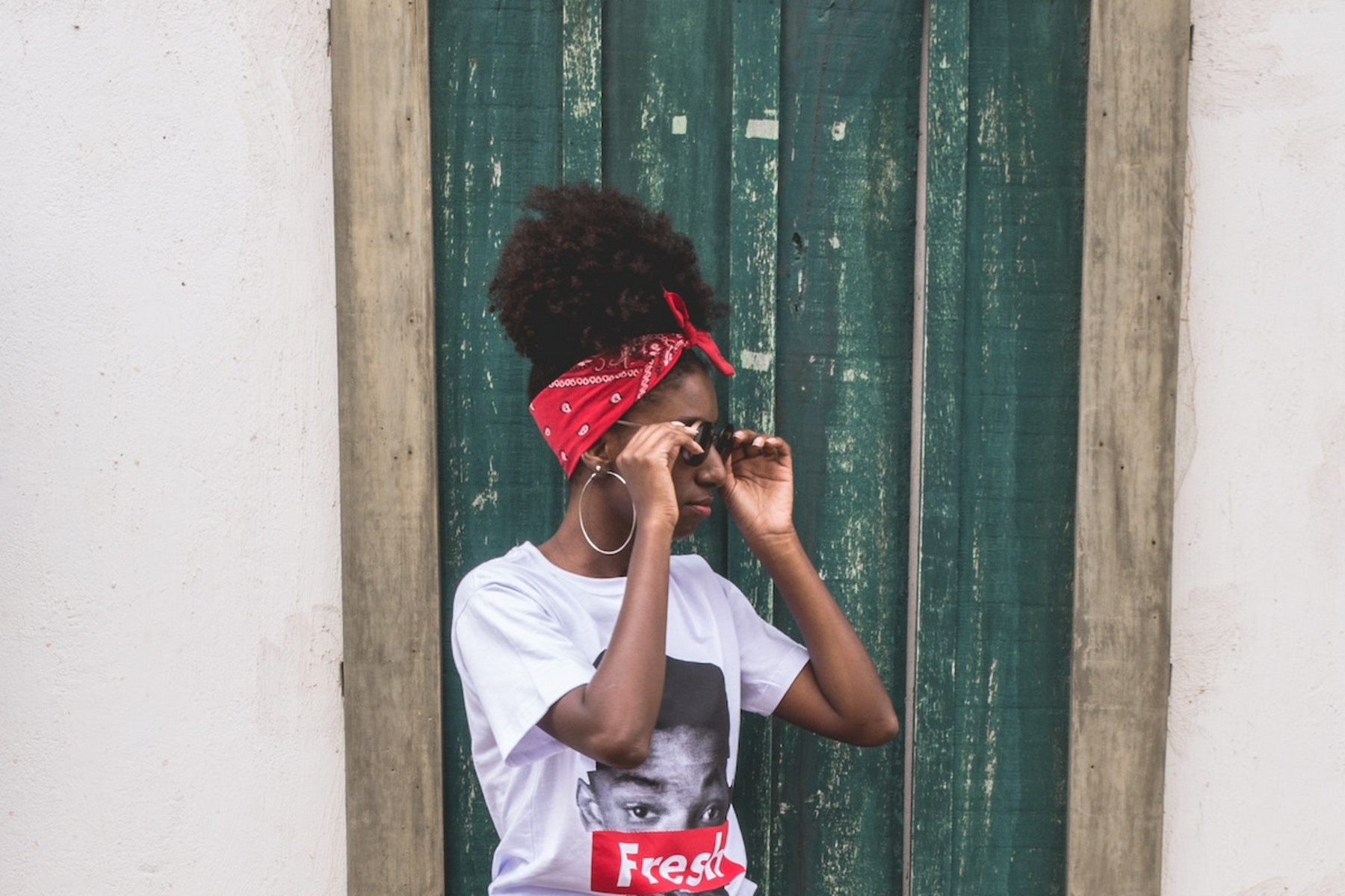 Eine Person mit einem Afro und einer Sonnenbrille steht vor einer grünen Tür.