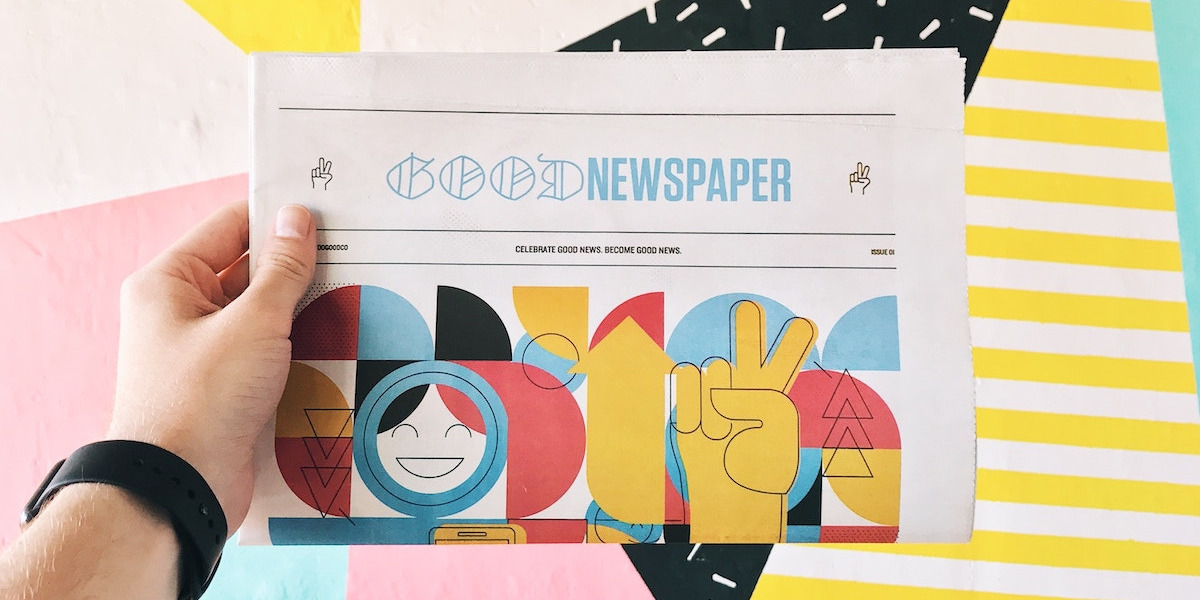 Zeitung "Good Newspaper" wird vor einem bunten Hintergrund gehalten