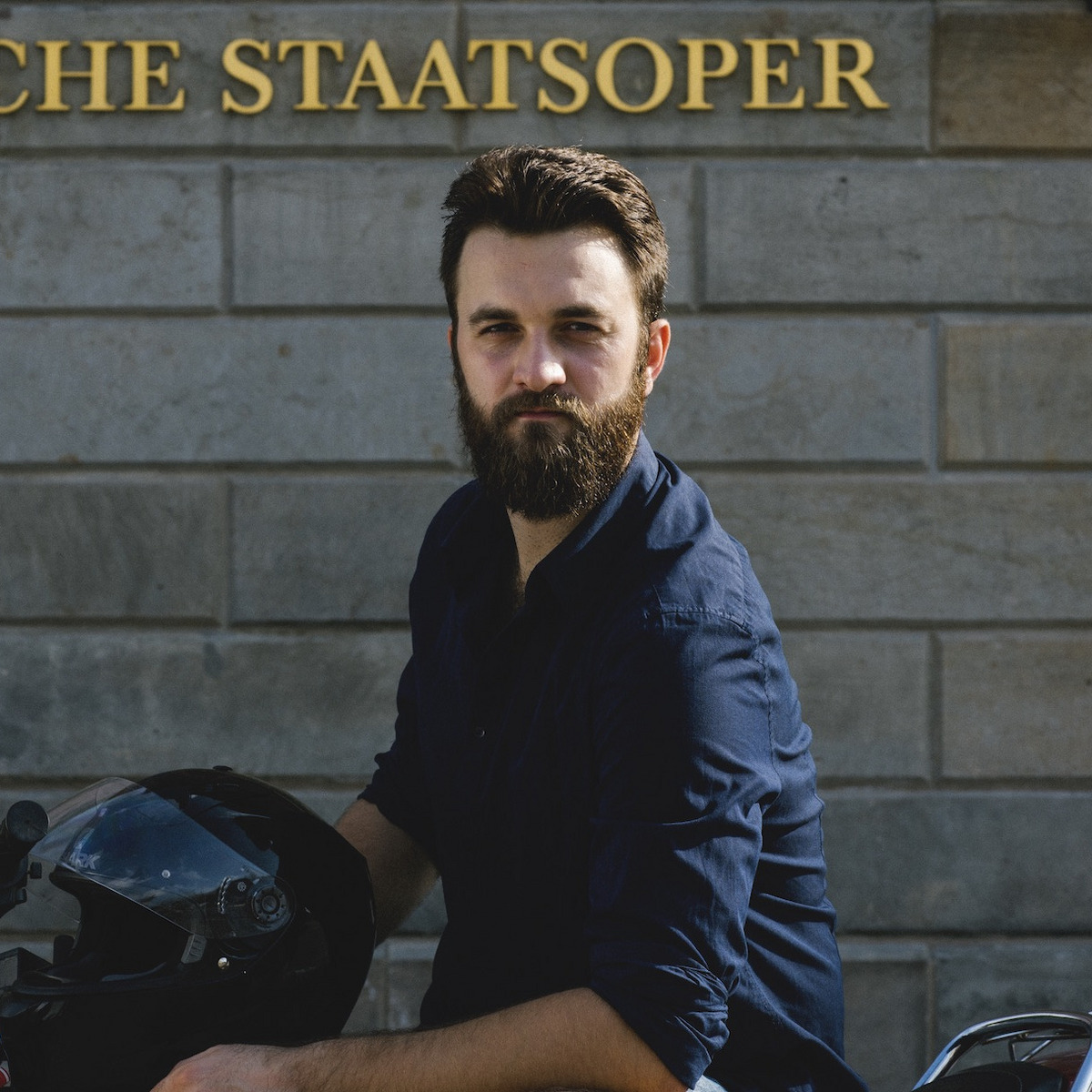 David Oštrek sitzt auf einem Motorrad vor der Staatsoper Berlin