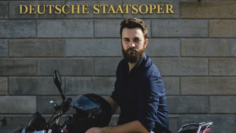 David Oštrek sitzt auf einem Motorrad vor der Staatsoper Berlin
