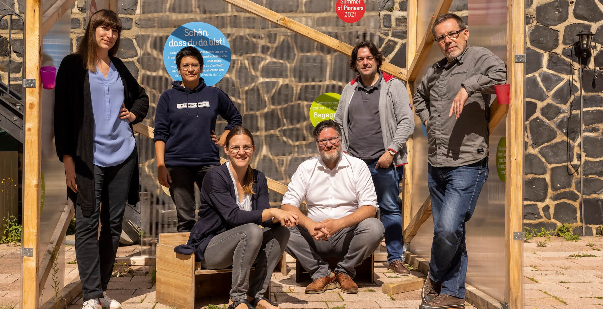 Das Foto zeigt sechs Personen, die für ein Gruppenfoto posieren. Es handelt sich um Teilnehmer:innen des "Summer of Pioneers", ganz links außen steht Sarah Ackermann.