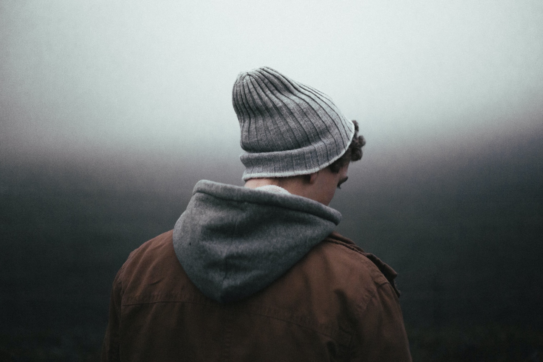 Ein Mann mit einer Strickmütze steht im Nebel und schaut auf den Boden.