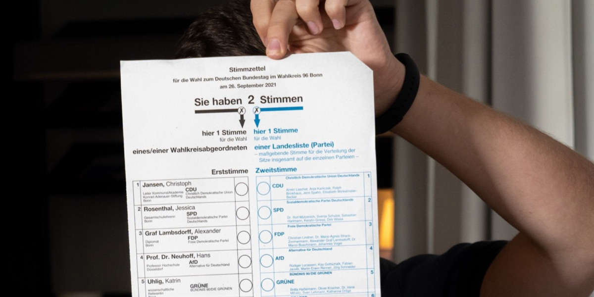 Eine Person hält einen Stimmzettel in die Kamera.