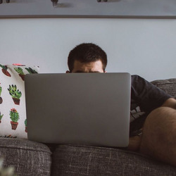 Ein Mann liegt auf der Couch vor seinem Computer.