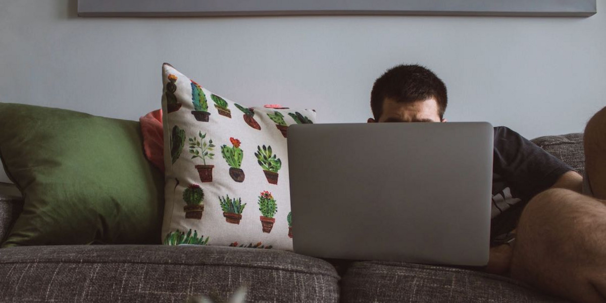 Ein Mann liegt auf der Couch vor seinem Computer.