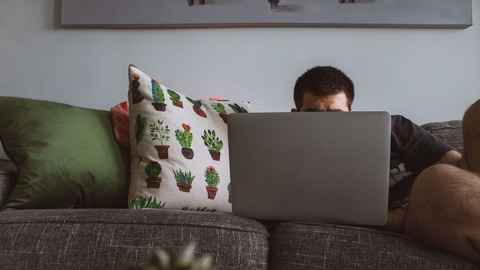 Ein Mann liegt auf der Couch vor seinem Computer.