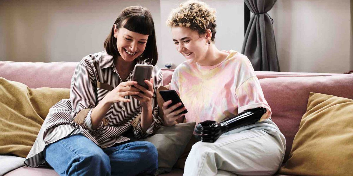 Zwei junge Frauen sitzen auf einem Sofa und schauen auf ihre Smartphones.