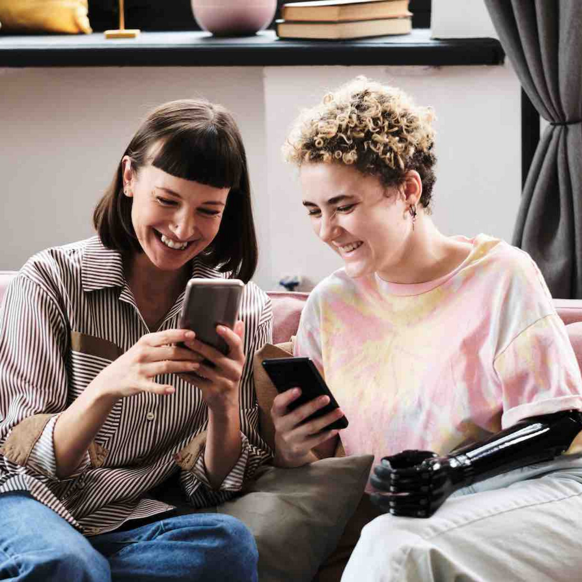 Zwei junge Frauen sitzen auf einem Sofa und schauen auf ihre Smartphones.