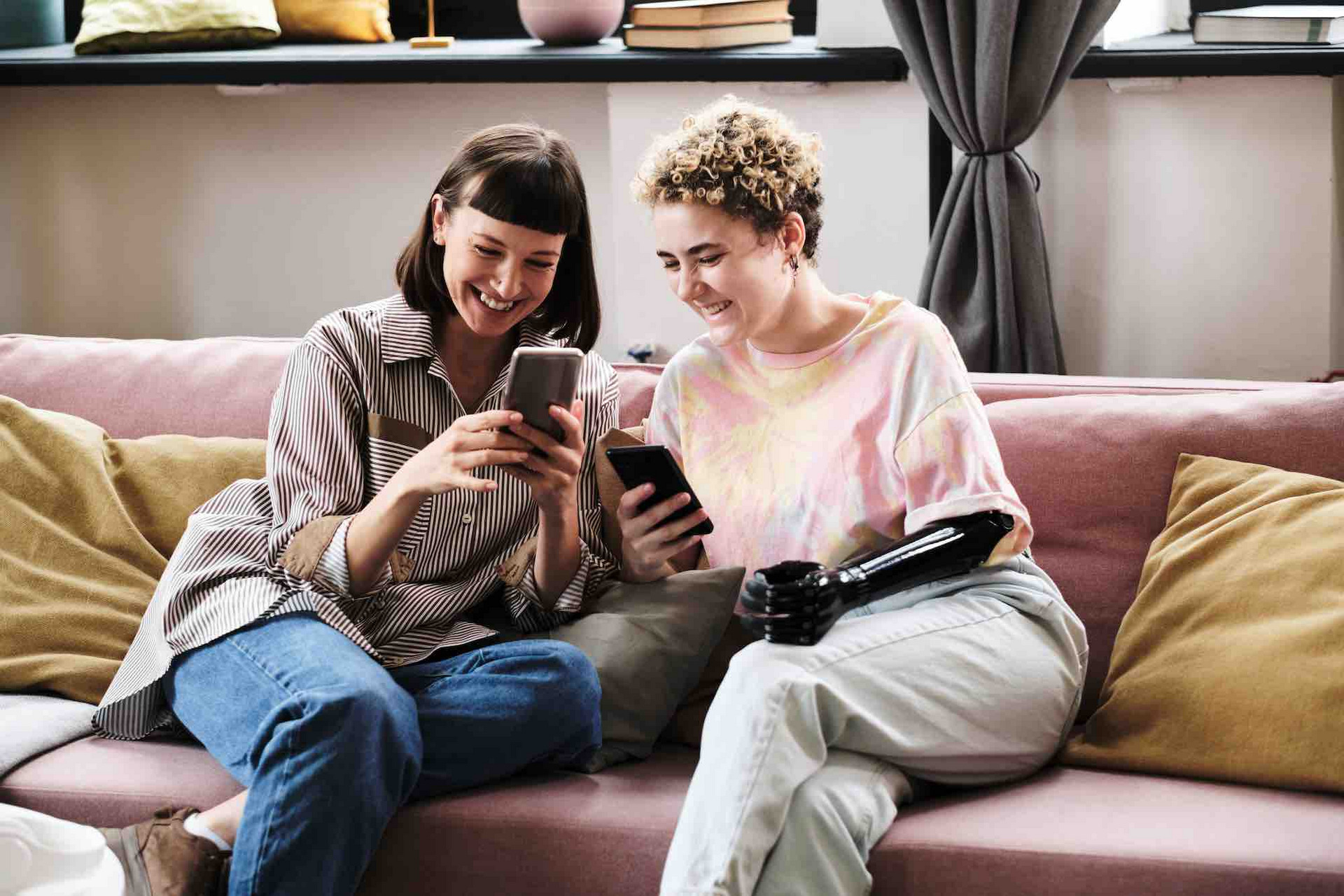 Zwei junge Frauen sitzen auf einem Sofa und schauen auf ihre Smartphones.