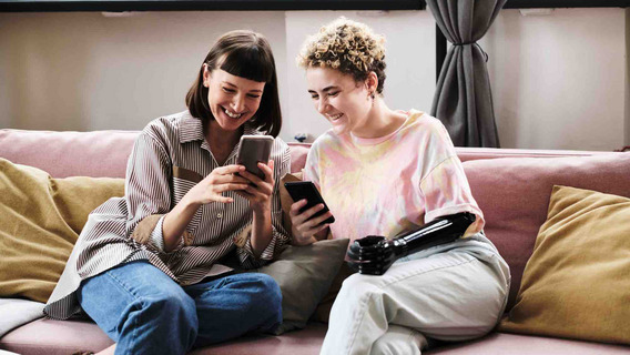 Zwei junge Frauen sitzen auf einem Sofa und schauen auf ihre Smartphones.